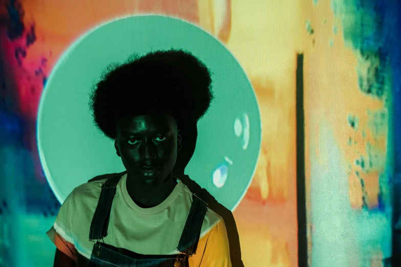 a man in overalls standing in front of a painting, pexels contest winner, afrofuturism, glowing aura around her, with afro, colour portrait photograph, vantablack wall