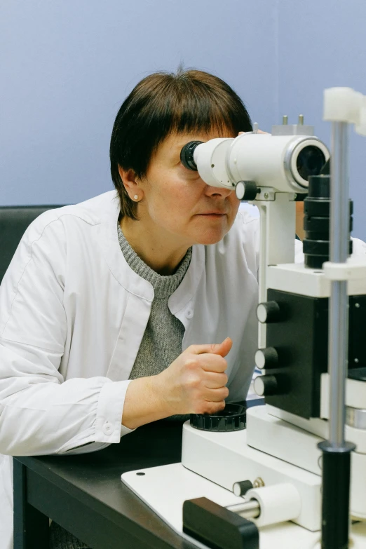 a woman sitting at a table looking through a microscope, a microscopic photo, by Maksimilijan Vanka, eye implants, academician prokhor zakharov, instagram photo, documentary photo