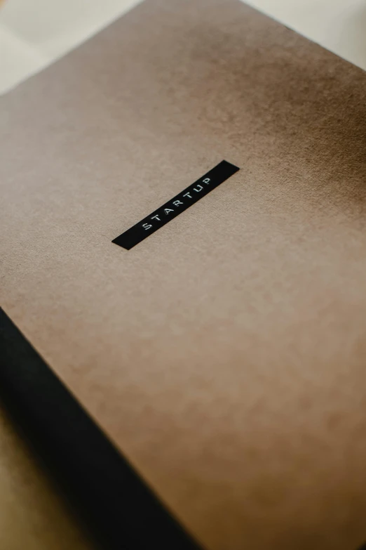 a laptop computer sitting on top of a wooden table, an album cover, by Carey Morris, unsplash, minimalism, brown paper, simple logo, luxury journal cover, thumbnail