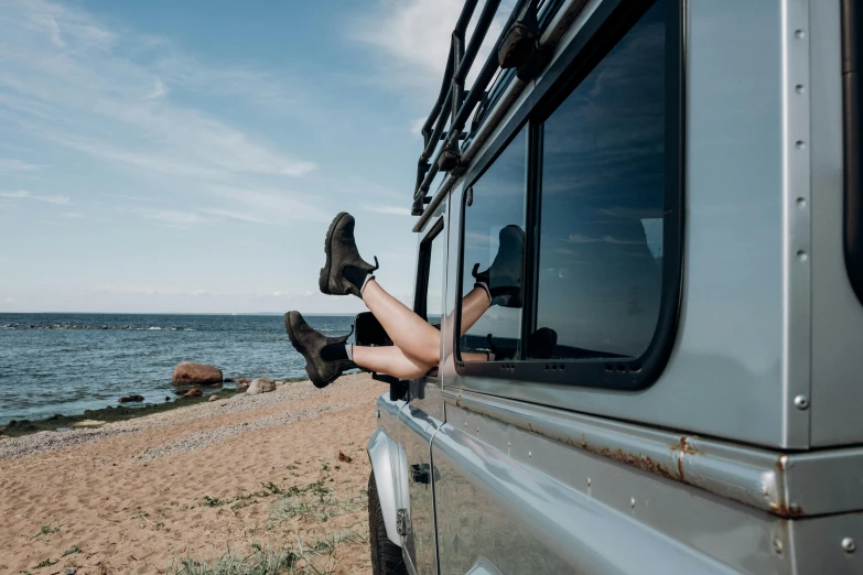 a woman's legs sticking out of the window of a vehicle, pexels contest winner, land rover defender, on the coast, relaxed expression, outside on the ground