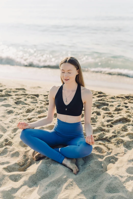 a woman sitting on top of a sandy beach, a portrait, by Julia Pishtar, unsplash, renaissance, meditating pose, low quality photo, wearing a black cropped tank top, lapis lazuli