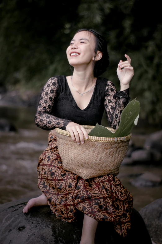 a woman sitting on a rock holding a basket, inspired by Ruth Jên, pexels contest winner, sumatraism, smiling and dancing, riverside, black, medium format. soft light