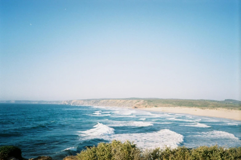 a large body of water next to a sandy beach, unsplash, happening, bulli, photographed on expired film, view from far away, cliff