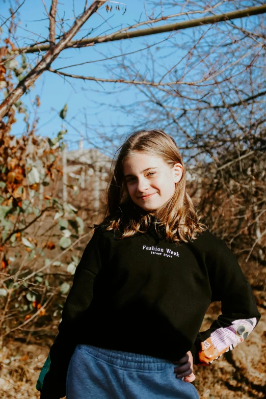 a woman standing in a field with a frisbee, an album cover, pexels contest winner, wearing a black sweater, greta thunberg smiling, foliage clothing, official store photo