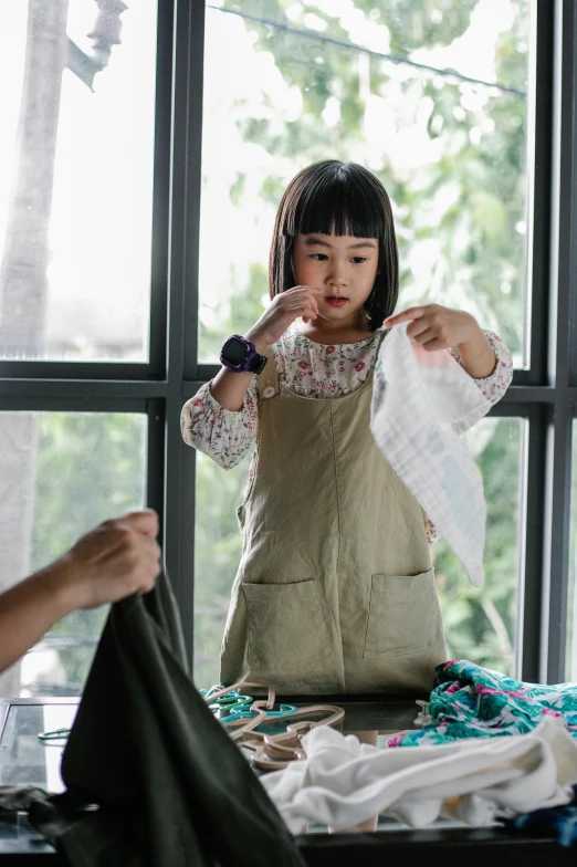 a little girl that is standing in front of a window, carefully crafted, an asian woman, wearing a shirt, utility