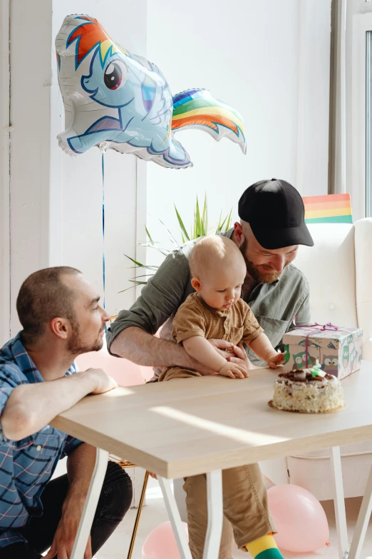 a man and woman sitting at a table with a baby, pexels contest winner, holding a birthday cake, lgbt, fatherly, cute boys