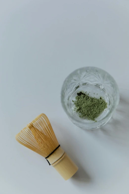 a whisk next to a glass of green tea, a picture, inspired by Kanō Shōsenin, trending on unsplash, face mask, powder, curated collection, with a white background