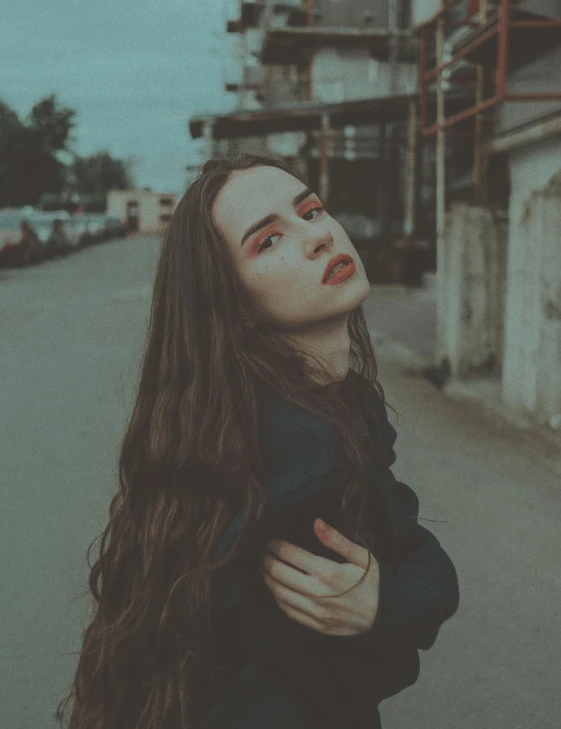a woman standing in the middle of a street, inspired by Elsa Bleda, trending on pexels, aestheticism, ilya kuvshinov with long hair, pale skin and dark eyes, desaturated color, satisfied pose