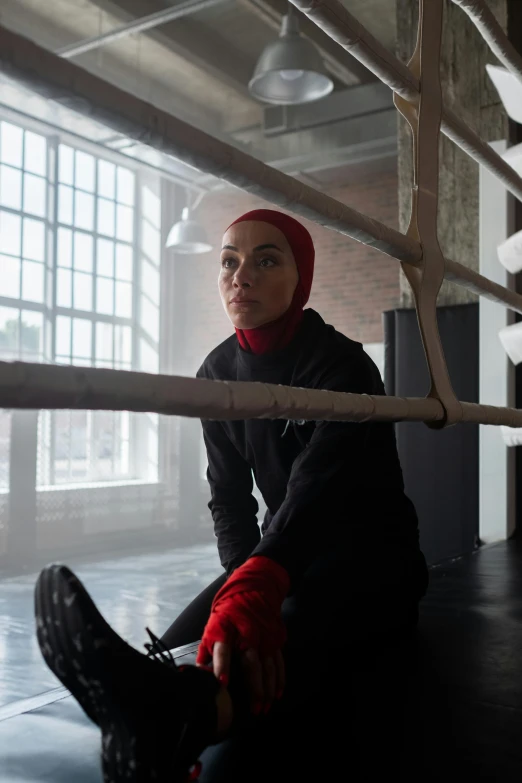 a woman sitting on the ground in a boxing ring, inspired by Louisa Matthíasdóttir, hurufiyya, black widow, wearing a scarlet hoodie, cinematic. ”, [ theatrical ]