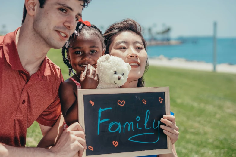 a family holding a chalk board with the word family written on it, a colorized photo, pexels contest winner, asian descent, standing near the beach, people on a picnic, an olive skinned