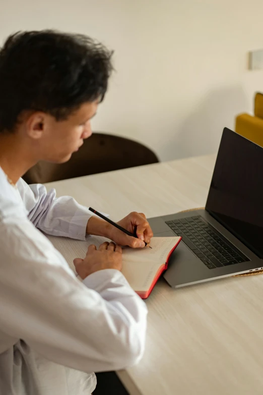 a man sitting at a table working on a laptop, by Nicolette Macnamara, pexels, male teenager, writing on a clipboard, thumbnail, multiple stories