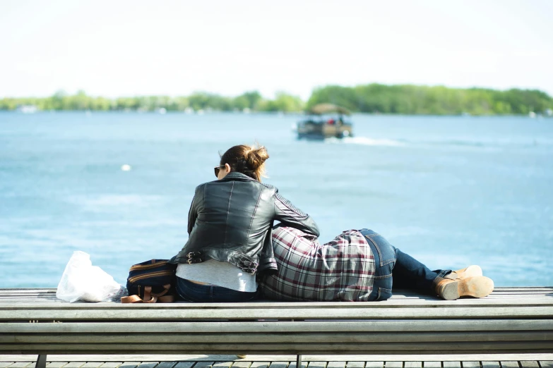a couple of people that are sitting on a dock, lesbian, bench, slightly sunny weather, cuddling