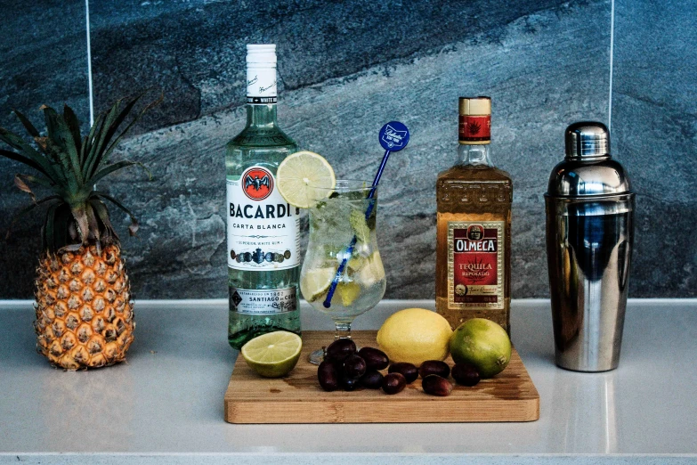 a bottle of alcohol sitting on top of a counter next to a pineapple, a still life, inspired by Ndoc Martini, featured on reddit, grey and blue theme, “the ultimate gigachad, ingredients on the table, at home