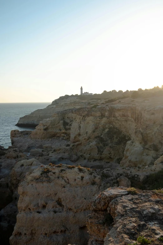 a man standing on top of a cliff next to the ocean, by Altichiero, les nabis, lighthouse in the desert, grotto, ibiza, sunset!