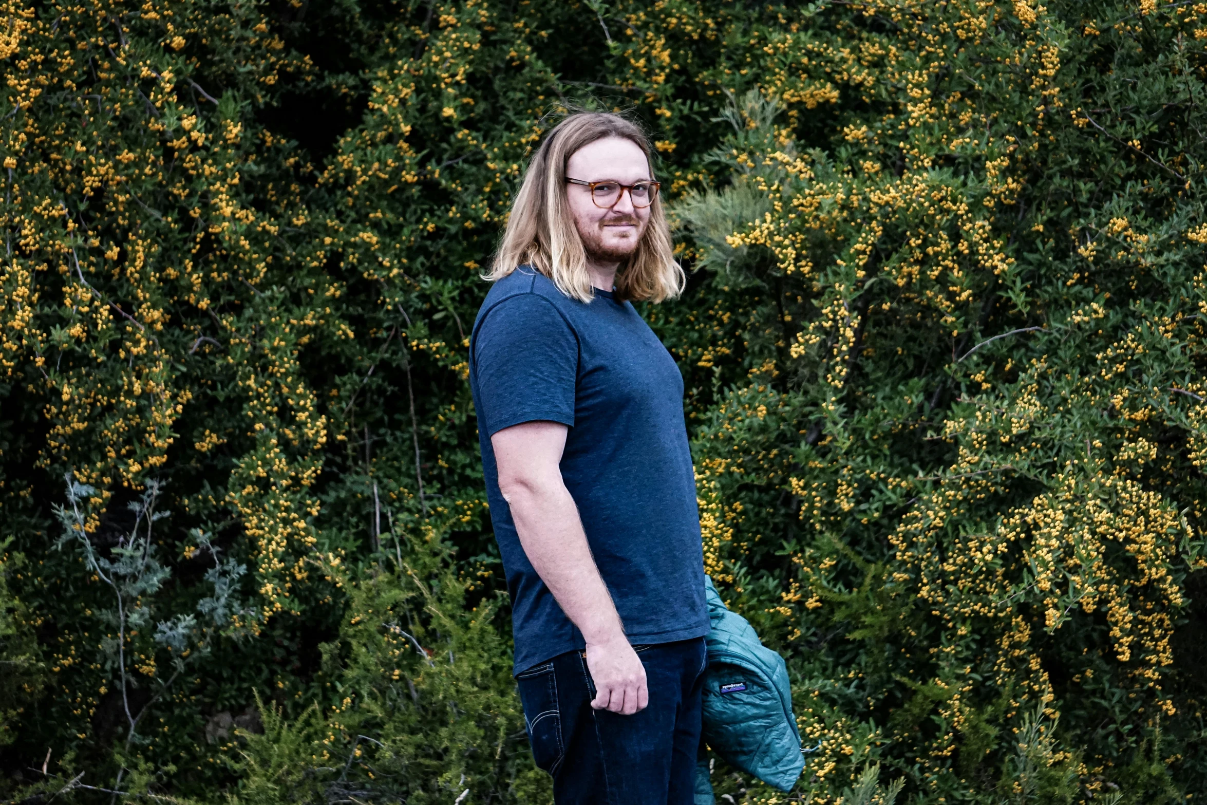 a man standing on a skateboard in front of a bush, a portrait, by Matthew Smith, unsplash, ginger bearded man with glasses, with long hair, profile image, bjørn skalldrasson