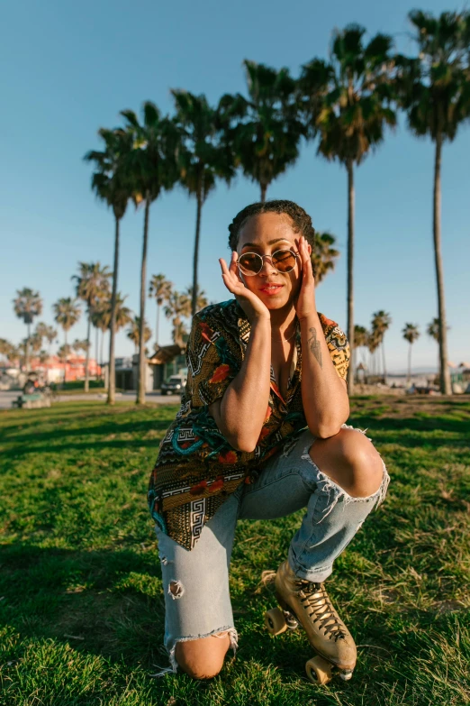 a woman sitting on top of a lush green field, with palm trees in the back, vanessa morgan, wearing gold glasses, in a beachfront environment