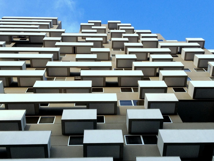 a tall building with lots of windows and balconies, a digital rendering, unsplash, brutalism, built on a steep hill, blue sky, parapets, fibbonacci