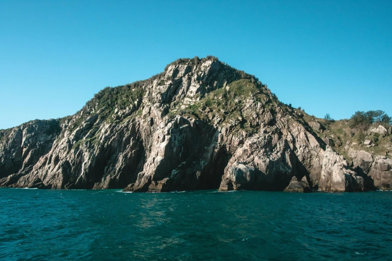 a large rock in the middle of a body of water, picton blue, steep cliffs, high-quality photo, fan favorite