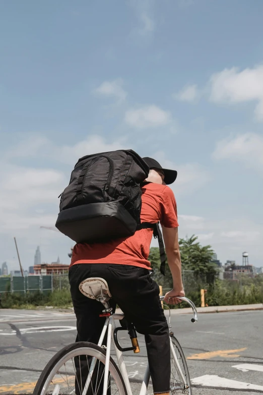 a man riding a bike with a backpack on his back, wearing a baseball cap backwards, ignant, black, super wide