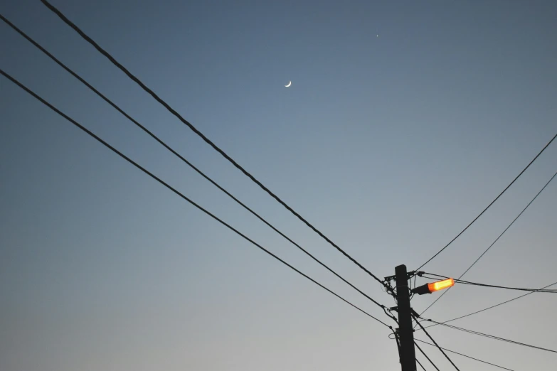 a street light sitting on the side of a road, inspired by Elsa Bleda, unsplash, postminimalism, crescent moon, telephone wires, ignant, low angle photograph