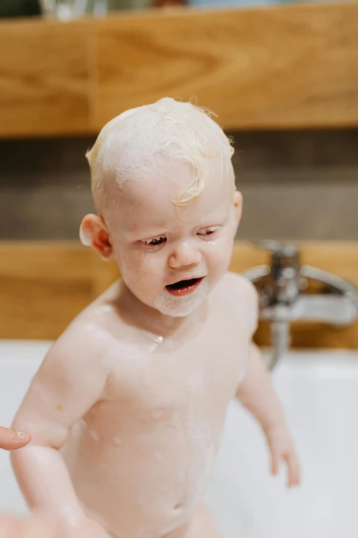 a person washing a baby in a bathtub, by Lee Gatch, pexels, process art, extremely pale blond hair, frosting on head and shoulders, young boy, soap