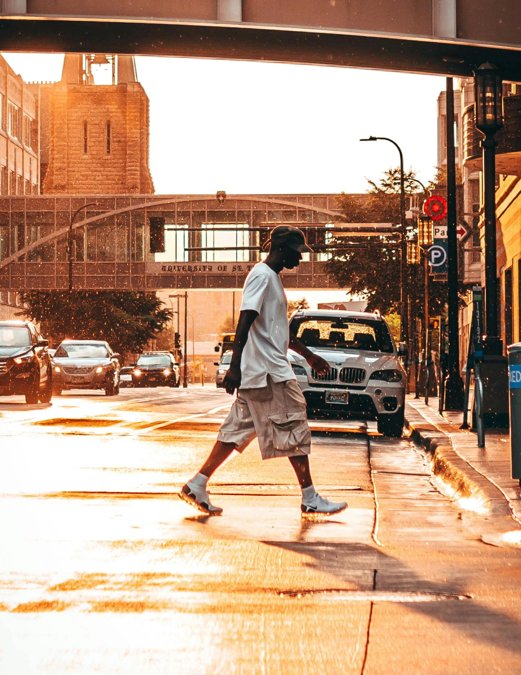 a man walking across a street under a bridge, unsplash contest winner, process art, handsome hip hop young black man, (golden hour), midwest town, summer rain