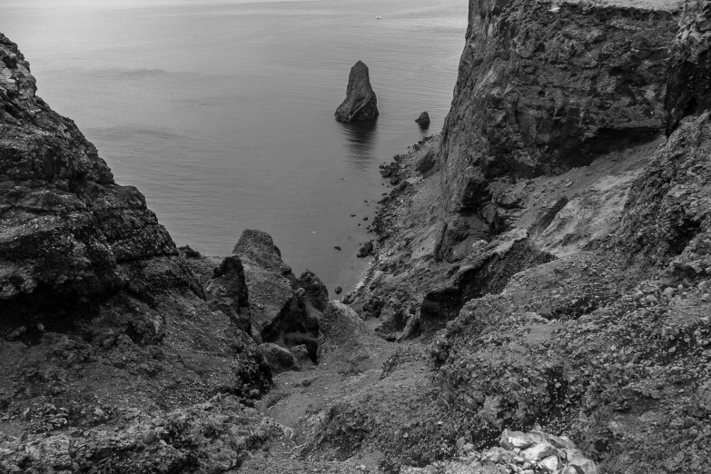 a black and white photo of some rocks and water, by Mathias Kollros, pexels contest winner, romanticism, steep cliffs, high angle vertical, distant hooded figures, haida