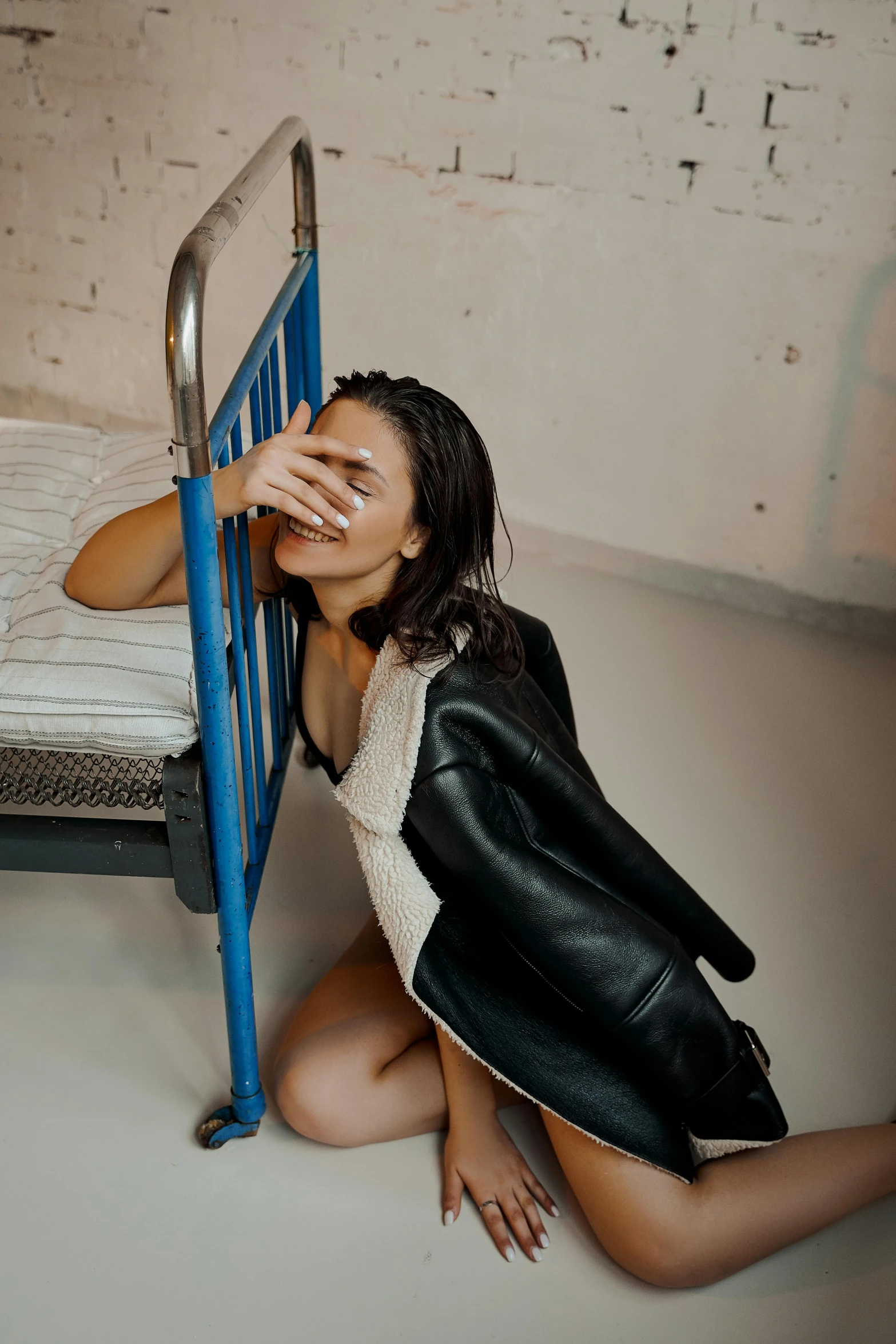 a woman sitting on the floor next to a bed, inspired by Elsa Bleda, trending on pexels, happening, wearing atsuko kudo latex outfit, crying and reaching with her arm, wearing leather coat, with a bunk bed