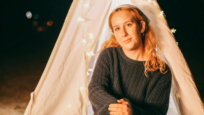 a woman sitting in front of a teepee at night, a portrait, inspired by Anna Findlay, unsplash, julia garner, slightly smiling, concert photo, emma uber