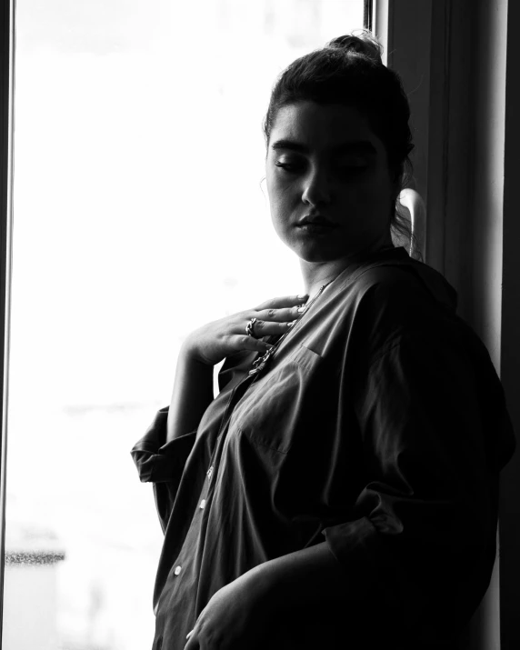 a black and white photo of a woman leaning against a window, a black and white photo, inspired by Max Dupain, unsplash, portrait of florence pugh, wearing a hospital gown, non binary model, expressive!!!!!