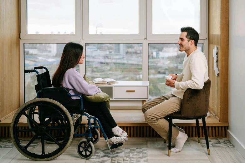 a man in a wheelchair talking to a woman in a wheelchair, by Julia Pishtar, trending on pexels, hurufiyya, looking out window, sitting on top a table, male and female, sitting on an armchair