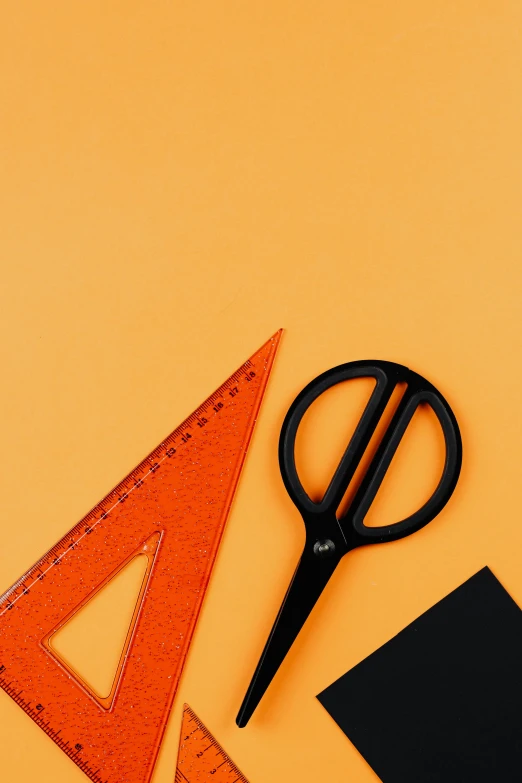 a pair of scissors sitting on top of a piece of paper, by Julia Pishtar, black and orange colour palette, educational supplies, triangle, objects