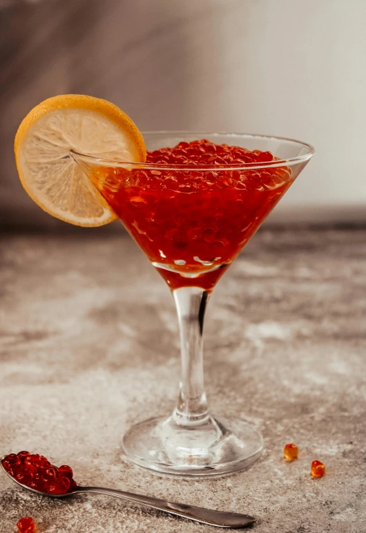 a martini sitting on top of a table next to a spoon, a portrait, inspired by Ndoc Martini, pexels, red caviar instead of sand, lemon, raspberry, premium