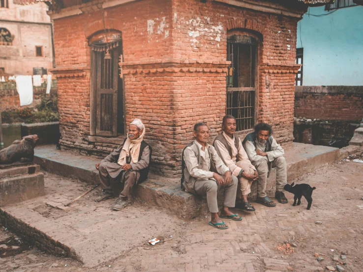 a group of men sitting in front of a brick building, pexels contest winner, nepali architecture buildings, background image, vintage color photo, ash thorp