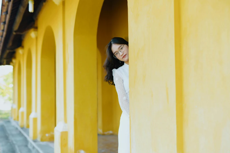 a woman in a white dress leaning against a yellow wall, by Tan Ting-pho, pexels contest winner, white stone arches, delightful surroundings, pale yellow wallpaper, white sleeves