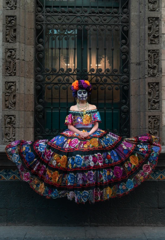 a woman in a colorful dress sitting in front of a building, inspired by Frida Kahlo, pexels contest winner, portrait of a holy necromancer, downtown mexico, square, dark ballerina