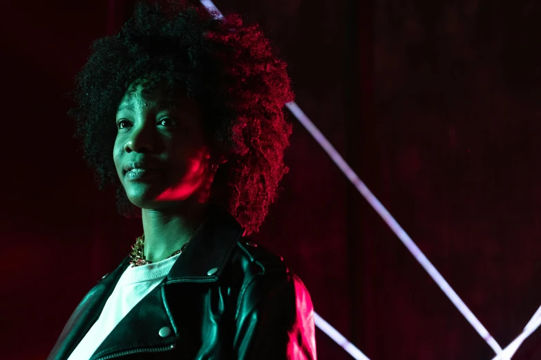 a woman standing in front of a red light, an album cover, pexels, afrofuturism, in a black room, afro hair, concert, actress