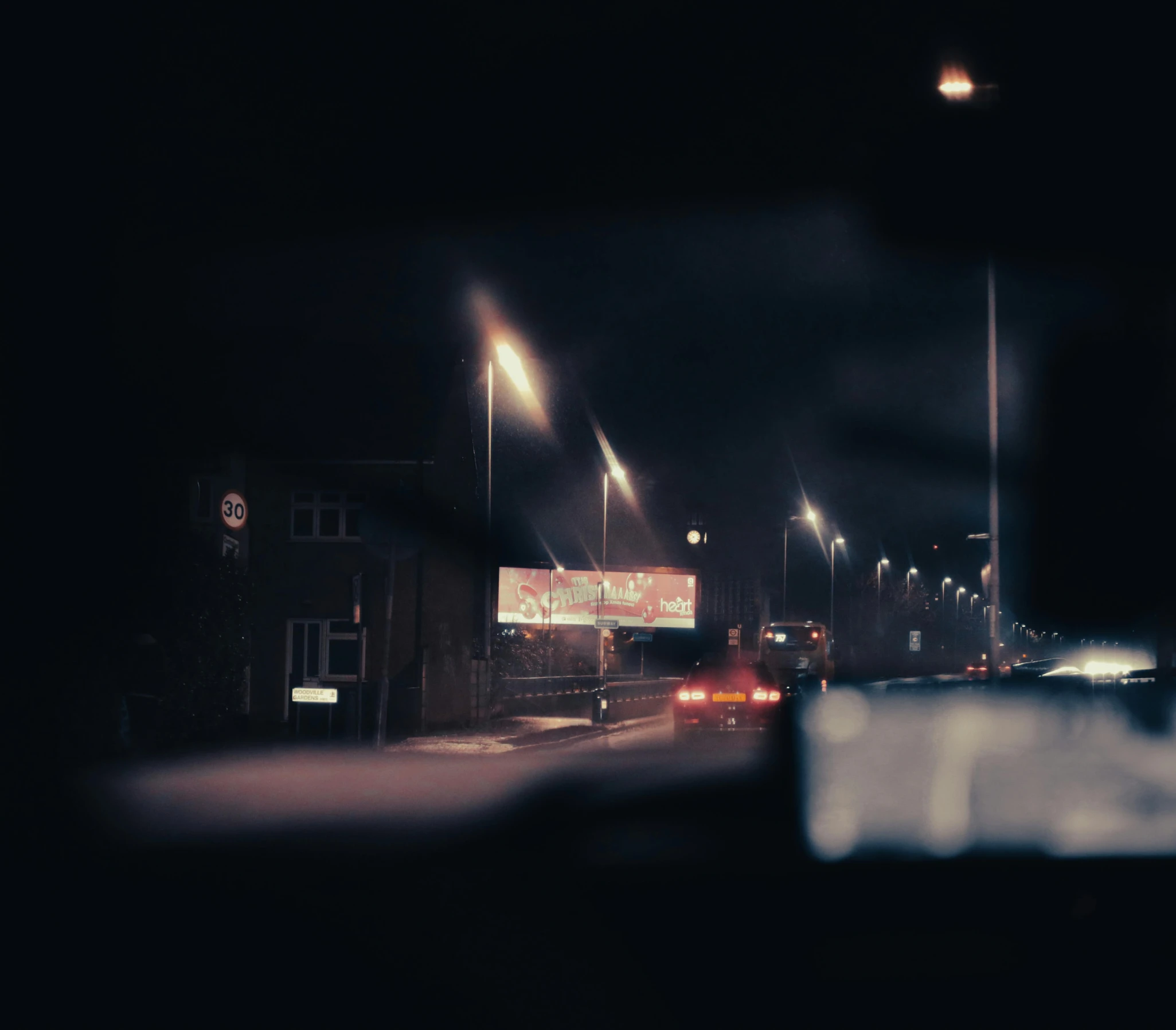 a car driving down a street at night, an album cover, unsplash, realism, silent hill streets, analogue photo, nightlife, suburb