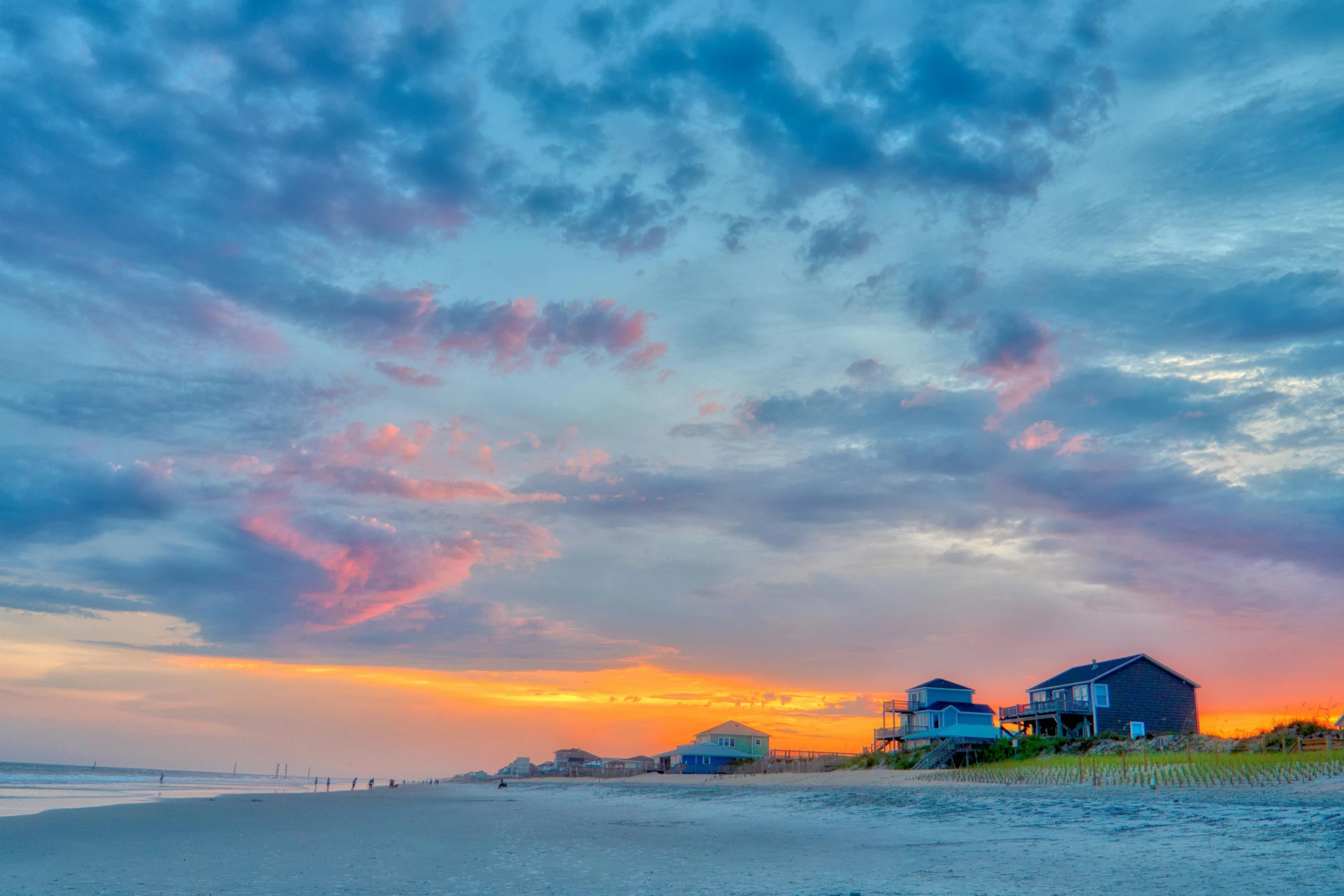 a couple of houses sitting on top of a sandy beach, by Carey Morris, pexels contest winner, sunrise colors, panoramic, fan favorite, cotton candy clouds