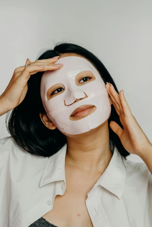 a woman putting a mask on her face, trending on pexels, asian face, on clear background, silicone skin, frontal pose