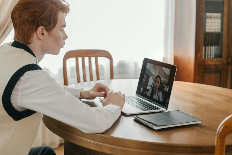 a man sitting at a table using a laptop computer, trending on pexels, video art, teenage boy, giving an interview, long distance photo, lachlan bailey