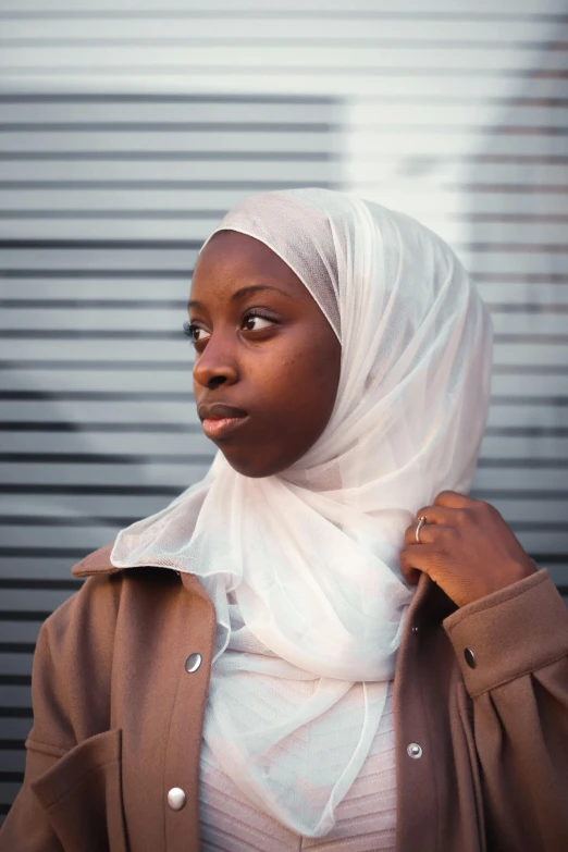 a woman wearing a brown jacket and a white scarf, inspired by Maryam Hashemi, trending on unsplash, black teenage girl, wearing translucent sheet, concerned, islamic