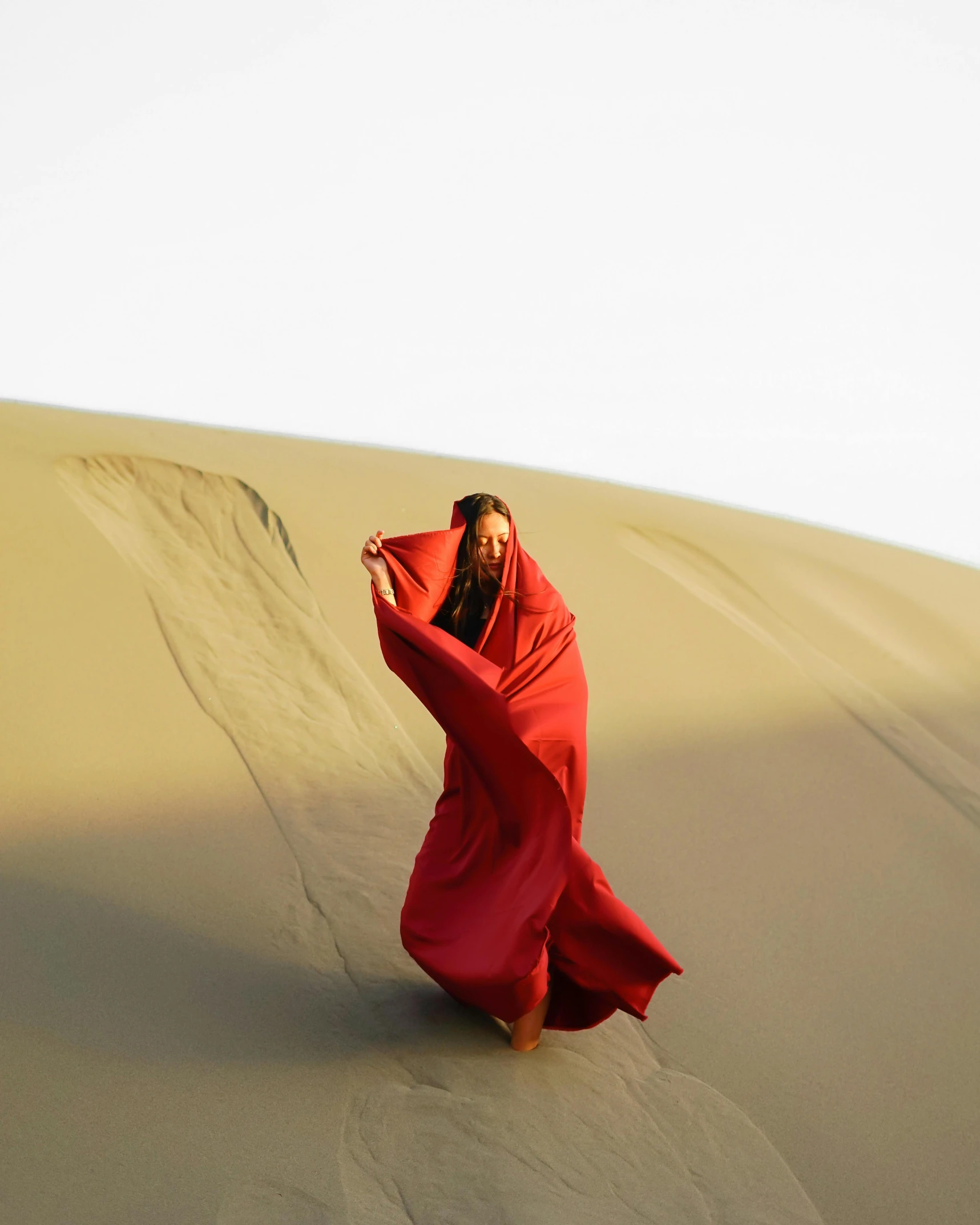 a woman in a red dress is walking on a sand dune, an album cover, unsplash contest winner, wears a long robe, disrobed, triumphant pose, songlines