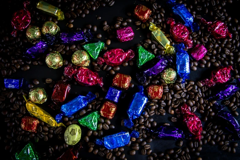 a pile of chocolates sitting on top of a pile of coffee beans, by Julia Pishtar, pexels contest winner, gold black and rainbow colors, high contrast plastic, drink, foil