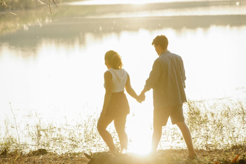 a man and a woman holding hands in front of a lake, sun behind her, profile image, sydney park, people walking around