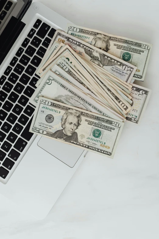 a laptop computer sitting on top of a pile of money, by Byron Galvez, trending on unsplash, 💣 💥💣 💥, flatlay, low quality photo, plain background