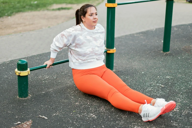 a woman sitting on the ground at a park, curvy crossfit build, white and orange, multicoloured, on a bridge