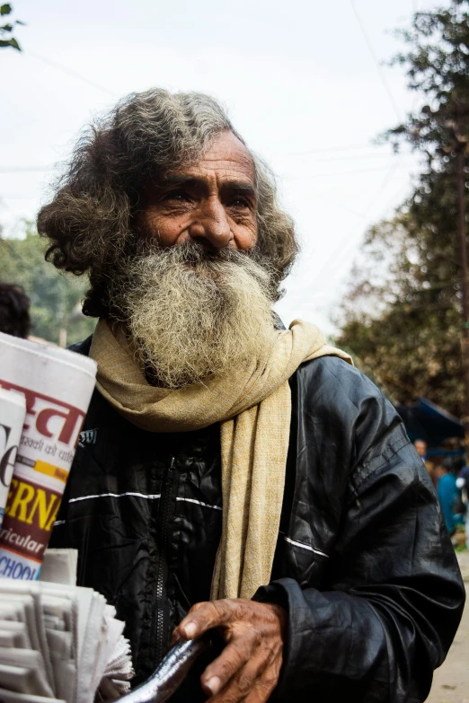 a man with a long beard holding a newspaper, pexels contest winner, bengal school of art, skilled homeless, warm friendly face, roadside, similar to hagrid