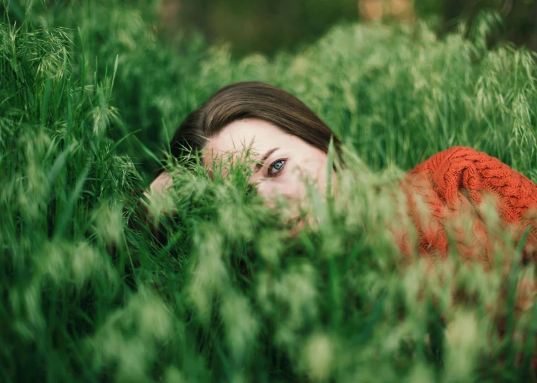 a woman laying in a field of tall grass, inspired by Elsa Bleda, pexels contest winner, hiding behind obstacles, red and green, looking into camera, avatar image