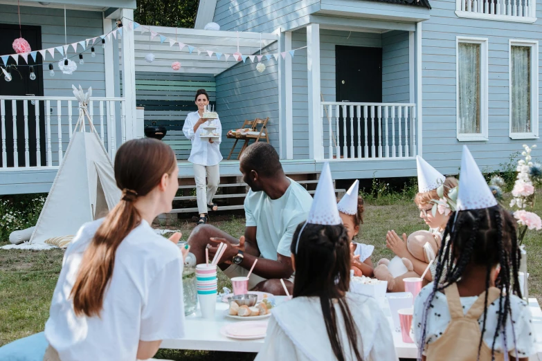 a group of people sitting around a table in front of a house, pexels contest winner, birthday party, white, people on a picnic, giving a speech